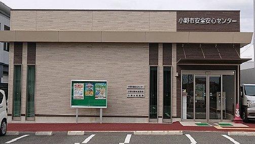 正面の右端に入口があり左の壁前に掲示板がたつ小野市安全安心センターの外観の写真