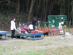 「遊び村」の玩具でそれぞれに遊ぶ二人の幼児とそれを見守る両親の写真