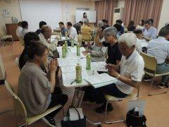 6名程度のグループごとに分かれテーブルを囲み資料を広げながら討議をする参加者たちの写真