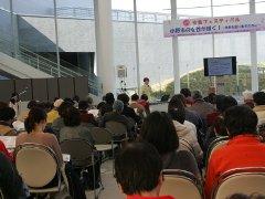 パイプ椅子に座りながら講演を聴くたくさんの人たちの写真
