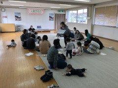 フローリングに敷かれたカーペットの上で会話を交わす母親同士と自由に動いている子供達の写真