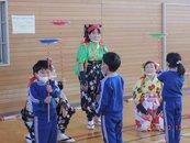 南京玉すだれの衣装を着た3人の女性の前で上手にお皿を回す男女3人の園児の写真