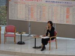 椅子に座り解説を行うスーツ姿の女性の写真