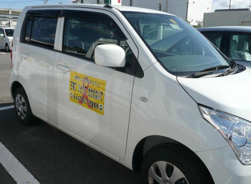 駐車場に止まっている、児童虐待防止啓発用のボディパネルが掲示された白い公用車の写真