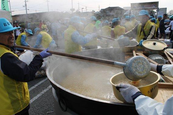 大きな鍋に入っている味噌汁を配っている写真