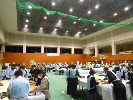 会場内で選挙開票事務員が青いゼッケンを着て開票作業を行っている様子の写真