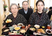 沢山の食事が乗ったお盆を持っている女性2人の写真
