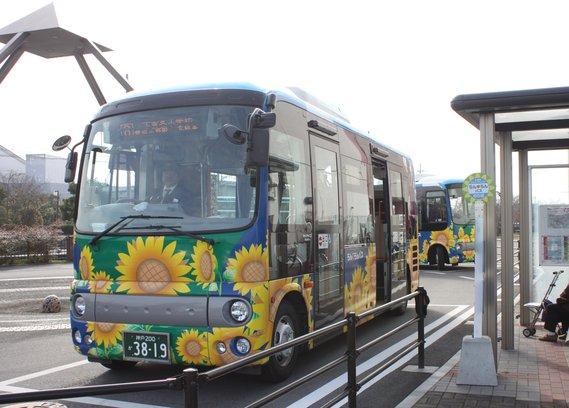 青地にひまわりがデザインされたらんらんバスが停留所に停車している写真