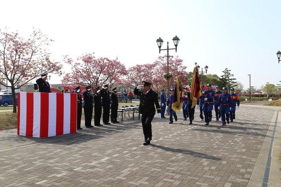消防員が敬礼し、道路を行進している平成29年度の小野市消防大会の写真