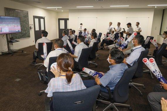 大型モニターの前で職員が田中選手の陸上5000メートル予選を応援している様子の写真