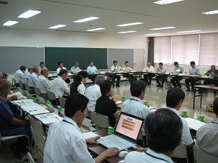 四角く並べられたテーブルにつき、資料などを見ながら話し合っている会議の写真