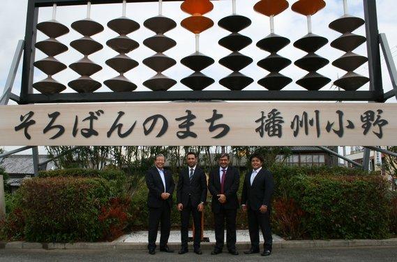 そろばんのモニュメントの前でスーツを着た男性4人が正面を向いて立っている写真