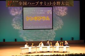 ステージの上で5人の人がテーブルにつき話し合っている写真
