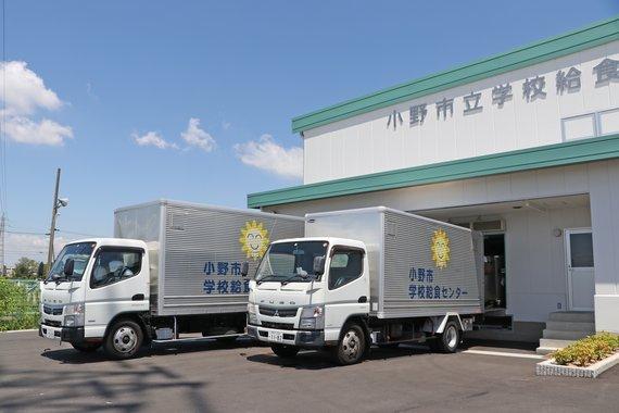 トラックが2台止まっている整備された新学校給食センターの写真