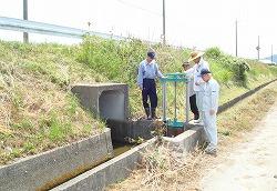 水路のある草地に立ち、施設の点検をしている人たちの写真