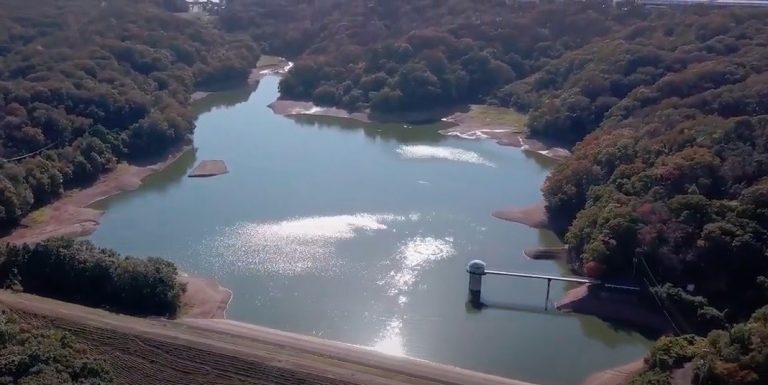 お寺の境内の前で、帽子にバックパックを身に着けた参加者の方々が集まり、説明を聞いている様子の写真