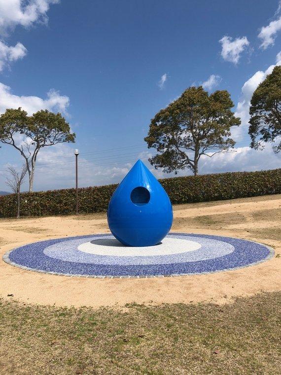 中央付近に穴が空いている青い雫状の水飲み場の正面を撮影した写真