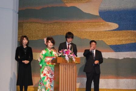 壇上のマイクの前に立つ新成人2人と手話をする男性、女性の写真