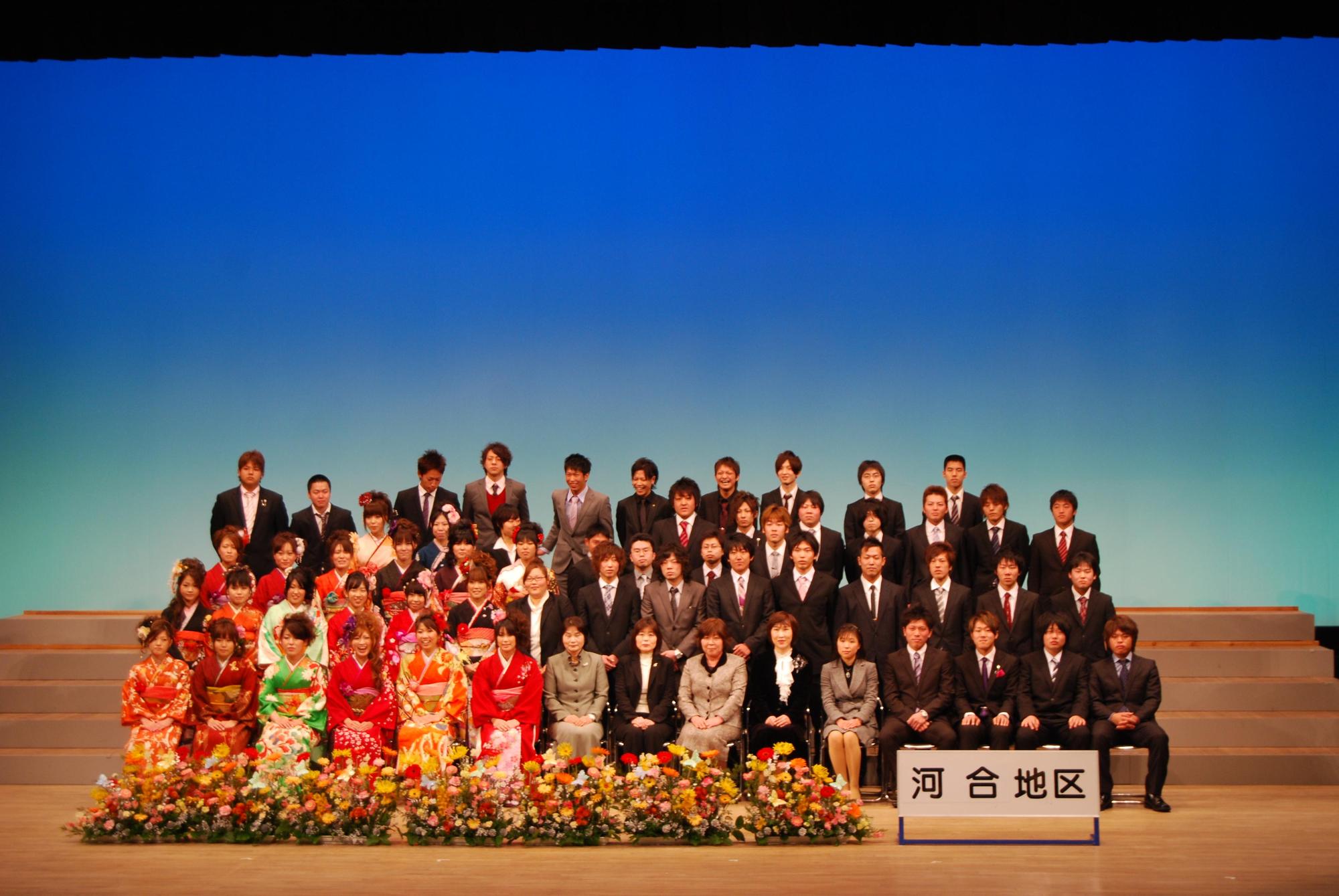 地区別の新成人の集合写真で河合地区のプレートの横にたくさんの花が置かれている写真