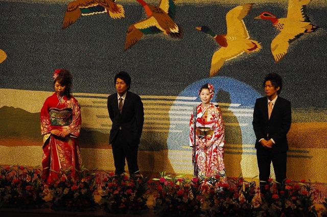 壇上で笑顔で話す新成人と、その話を真剣な表情で聞く3人の新成人たちの写真