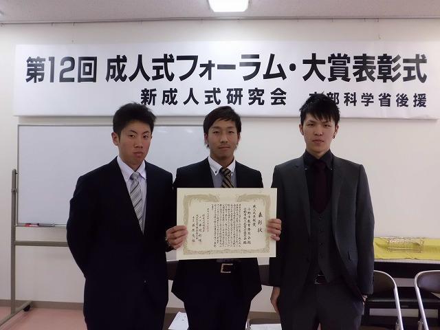成人式貢献賞の賞状を広げて並ぶ三人のスーツ姿の男性の写真