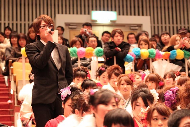 晴れ着姿の新成人と立席してコメントをするスーツ姿の新成人の写真