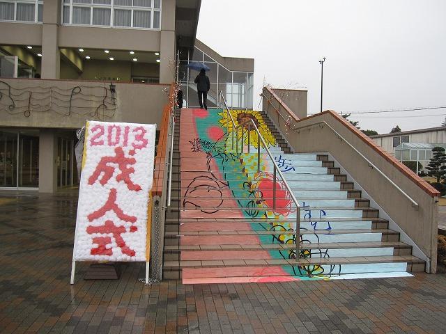 「2013 成人式」と書かれた看板と、ひまわりと赤と青の絵に彩られた階段アートの写真