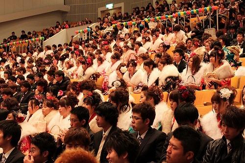 晴れ着姿の新成人達が席に座ってスクリーンを眺める写真