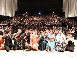 席に座った新成人達を背景に壇上に上がって座り並ぶ実行委員達の集合写真