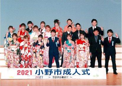 成人式に集まった笑顔でピースをするスーツの6人の男性と13人の着物姿の女性の写真
