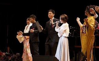 壇上で白服のシンガーソングライターcyan氏の歌唱に合わせ手拍子する実行委員達の写真