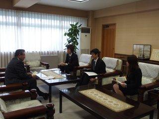 市長室でテーブル越しに面談する市長とスーツ姿の実行委員三人の写真