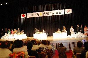 会場のステージ上に大量のビニール袋に入ったボトルキャップと新成人が写っている写真