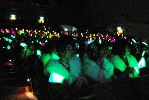 会場にて振袖を身にまとっている女性新成人たちが、ペンライトをかざし合唱している写真