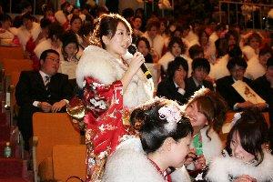 会場の座席からマイクを持って立ち上がる、振袖を身にまとった女性新成人の写真