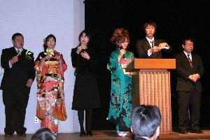 会場ステージ上で振袖を身にまとっている女性、スーツ姿の男性新成人が立っている写真