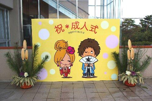 大人の階段を上った新成人を迎える新成人の男女をかたどったイラストの看板と両側の角松の写真