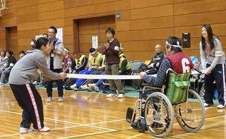 体育館内で車椅子がゴールテープを切ろうと走っている様子の写真