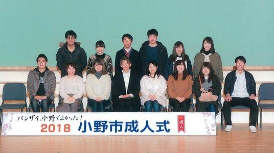「2018小野市成人式」と書かれたタイル帯の後ろに2列横に並んでいる実行委員達の写真