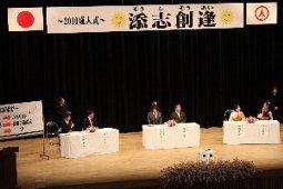 添志創逢の横断幕が掲げられた3組のパネリストたちの座る舞台の俯瞰写真