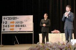 サイコロの目により発言者が変わる事を示すホワイトボードと前に立つ新成人、スーツの女性の写真