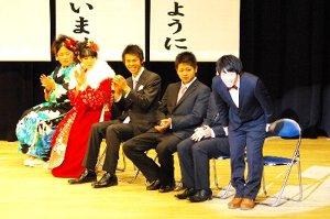 ハタチの短歌を背景に笑顔でお辞儀をする新成人と手を叩く壇上の新成人