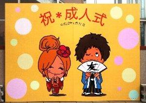 振り袖の女性と友の文字の扇子を持つ袴姿の男性のイラストと祝成人式と書かれた看板の写真