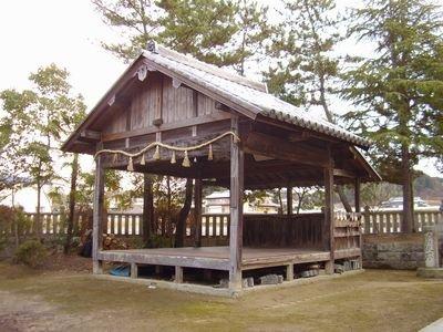木々の間に立つ、木造の垣田神社の能舞台の写真