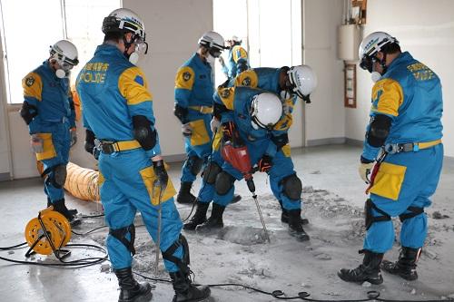 青い防護服を着た隊員たちがドリルを持ち階下層へ行くための穴を掘っている写真