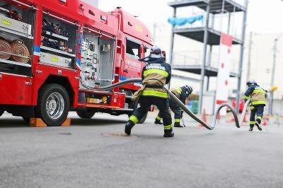 消防車の傍で消防隊員たちが消火訓練を行っている写真