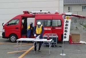 赤色の自動車の前に立つ黄色いベストを着た作業員の写真