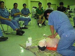 青い服を着た人が心肺蘇生人形を使って胸骨圧迫を行っている写真