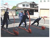 3人の消防隊員が巻かれたホースを伸ばしている写真