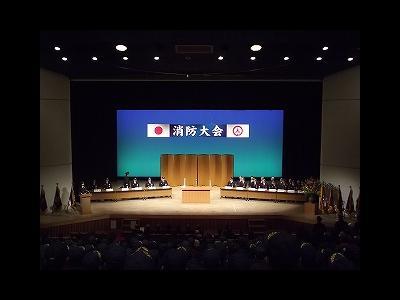 消防大会と書かれた横断幕が掲げられた会場に人が集まっている写真